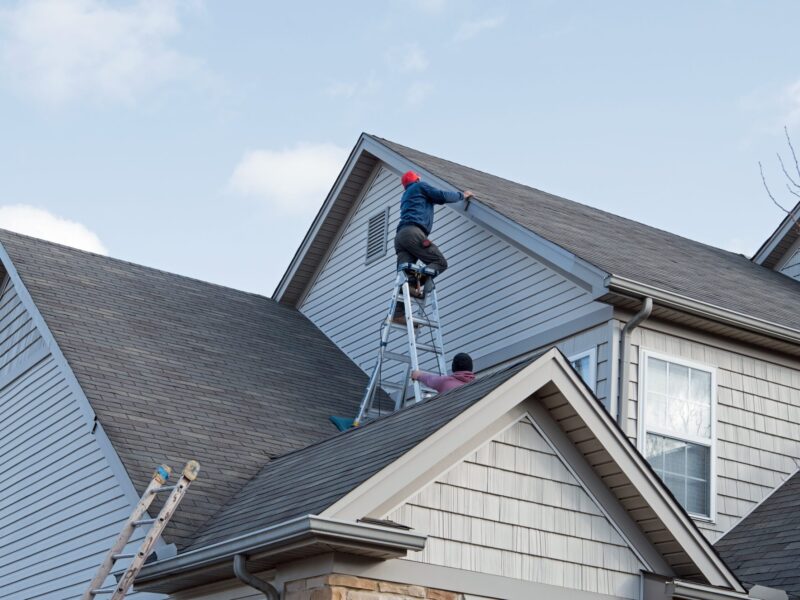 Roofers,Repairing,Damaged,Siding,Trim,Along,Multiple,Roof,Lines,From